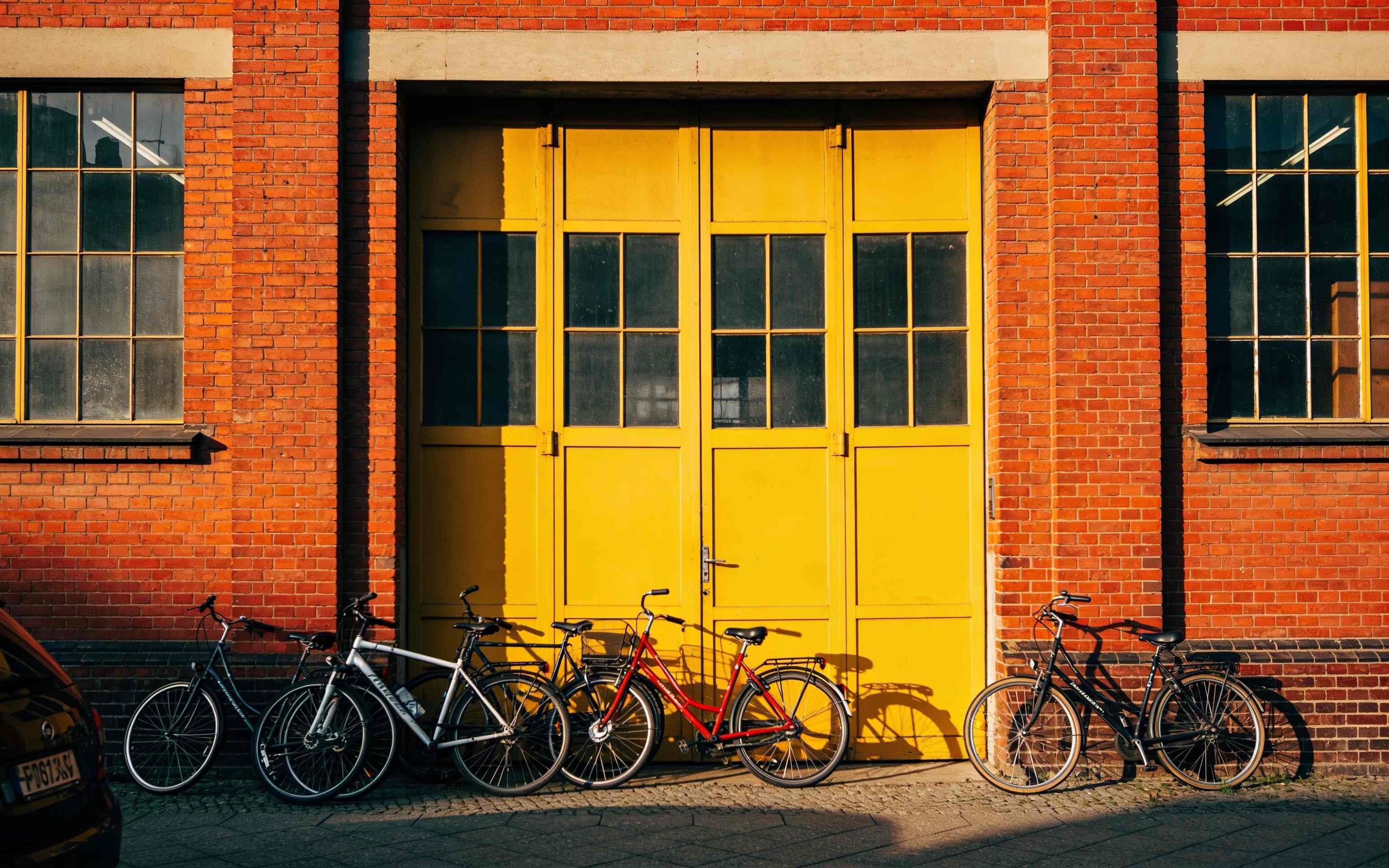 The red brick front of a converted factory with a big yellow door and bikes parked outside